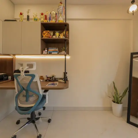 A compact wall-mounted study nook with open wood shelving displaying trophies and books, an ergonomic mesh chair