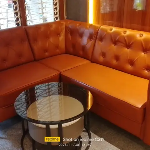 A corner sectional in tufted burnt-orange leather with a round glass coffee table set against dark wood-panelled walls and a metal-grille window.