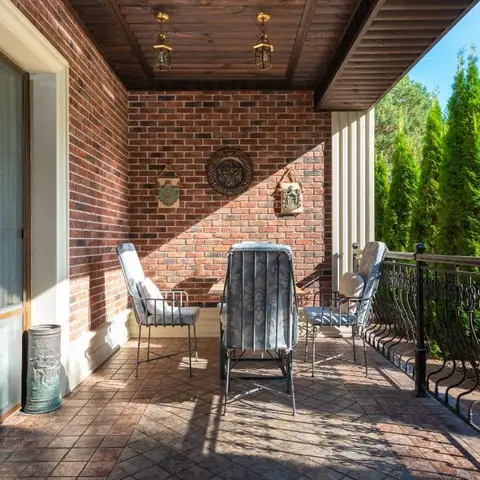 A covered terrace with an exposed brick accent wall, wrought-iron railing, wood plank ceiling with lantern pendants