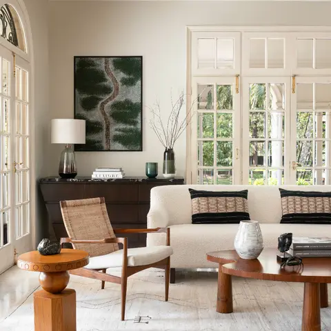 A cream boucle sofa and woven-back armchair around a curved walnut coffee table, with arched French doors opening onto a garden.