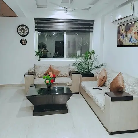A cream L-shaped sofa with tan cushions and a dark wood coffee table sit under a simple pop ceiling with a ceiling fan and framed art on the wall.