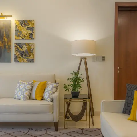 A cream living room with mustard-and-grey patterned cushions on two sofas, a wood tripod floor lamp