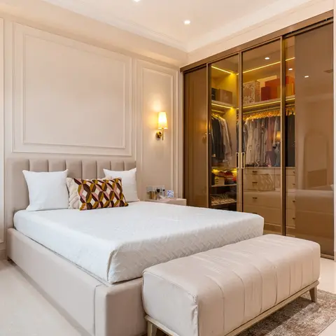 A cream panel-moulded master bedroom with a tufted upholstered headboard, brass wall sconces, an upholstered bench at the foot of the bed