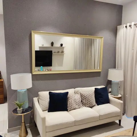 A cream three-seater sofa with navy and honeycomb-pattern cushions sits beneath an oversized gold-framed mirror on a textured grey wallpaper wall