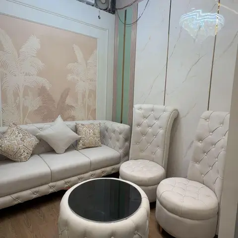 A cream tufted sofa and matching high-back chairs surround a tufted ottoman coffee table beneath a tiered crystal chandelier