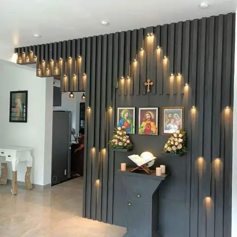 A dark fluted-panel prayer altar wall with integrated fairy lights, a wall-mounted cross, framed religious images and a podium stand with a Bible and candles.