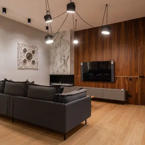 A dark grey sofa faces a wood-panelled feature wall with a wall-mounted TV and a built-in fireplace clad in white-veined marble