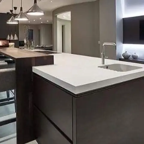 A dark modular kitchen island with a white quartz waterfall countertop and integrated sink, lit by three drum pendant lights