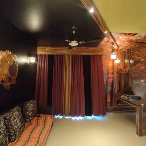 A dark-walled lounge with an autumn forest-mural wallpaper feature, rust drape curtains under a wood-beam ceiling trim