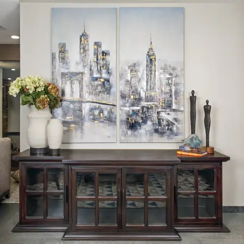 A dark wood console table styled with ceramic vases and bronze figurines beneath a large two-panel cityscape painting, set on a patterned rug.