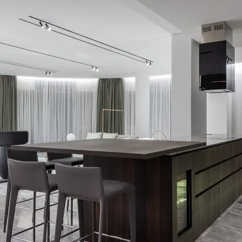 A dark wood-veneer kitchen island with grey leather bar stools and a floating cube-shaped chimney hood