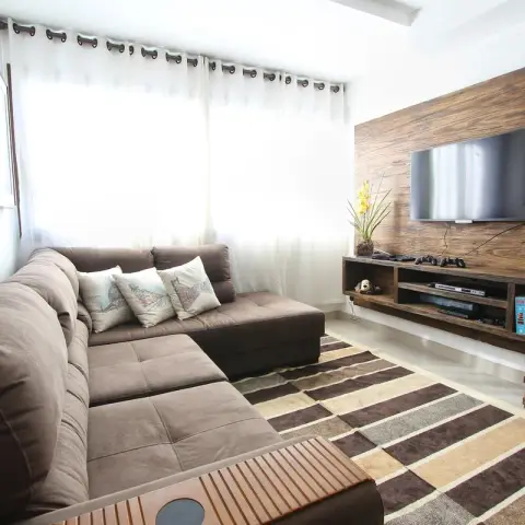 A deep brown L-shaped fabric sofa with three printed cushions faces a reclaimed-barnwood TV panel and a matching wall-hung open media console