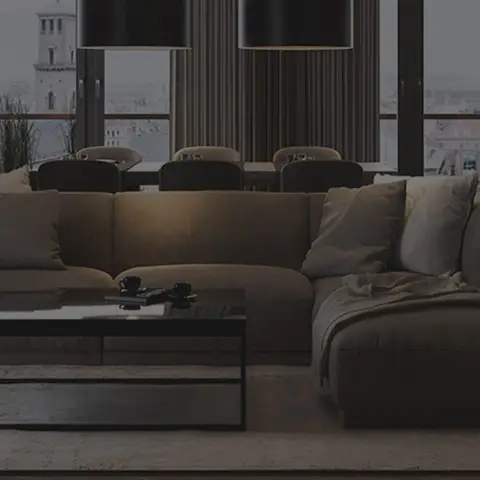 A dimly lit open-plan living area with a large taupe sectional sofa, black-framed glass coffee table, herringbone wood floor and fluted wall panelling