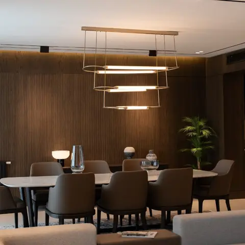 A dining area against a full-height fluted wood-panelled wall, lit by a stacked three-tier linear pendant fixture over an eight-seat table.