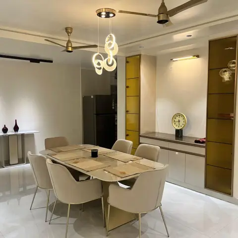 A dining nook with a marble-top table and cream chairs on brass legs, a ring-shaped bubble pendant chandelier overhead
