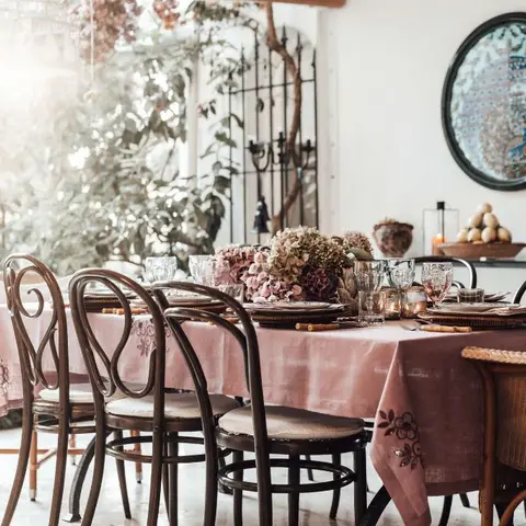 A dining nook with a mixed set of bentwood and wicker chairs around a table dressed in dusty-pink linen, a hydrangea centerpiece