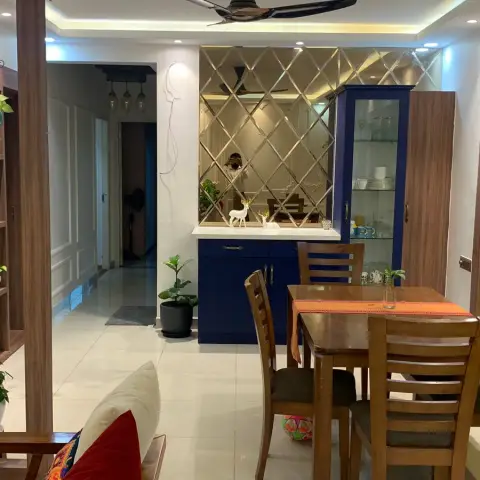 A dining nook with a wooden table set against a navy blue crockery cabinet topped with a diamond-mirror backsplash and deer figurine decor.