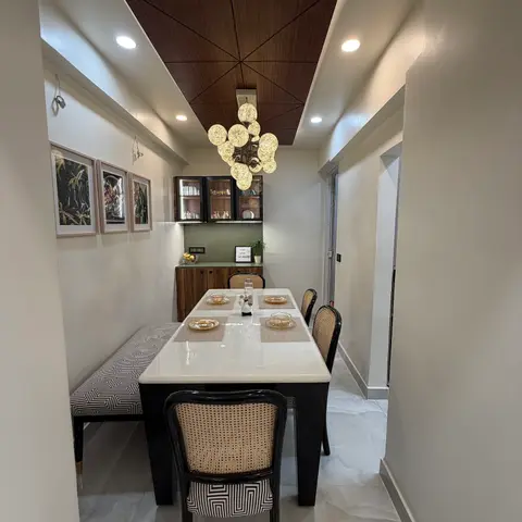 A dining nook with an angled walnut-panel ceiling feature, a bubble chandelier, cane-back black dining chairs, a graphic-pattern bench