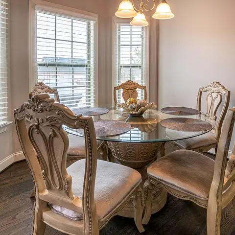 A dining nook with an ornately carved wood dining set featuring a round glass-top table and upholstered chairs