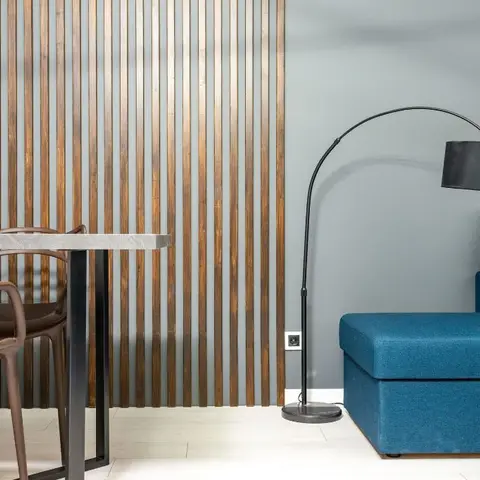 A dining nook with translucent modern chairs sits beside a wood-slat accent wall, next to a navy sectional sofa under a black arc floor lamp.