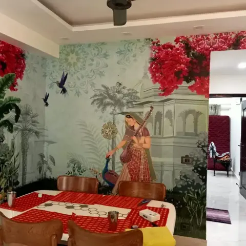 A dining room with a floor-to-ceiling Rajasthani-themed mural wallpaper of a woman playing veena among peacocks and palms.