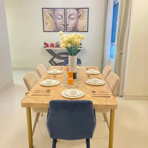 A dining room with a marble-top gold-legged table set for six, navy and cream velvet chairs, and a Buddha-face diptych above a console table.
