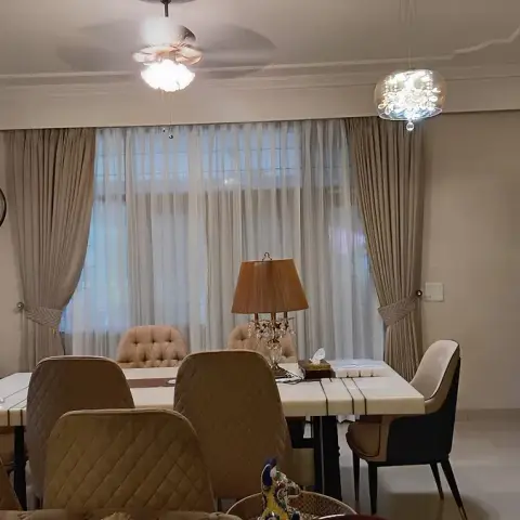 A dining room with a marble-top table surrounded by quilted upholstered chairs, twin crystal pendant lights, sheer-and-drape curtains