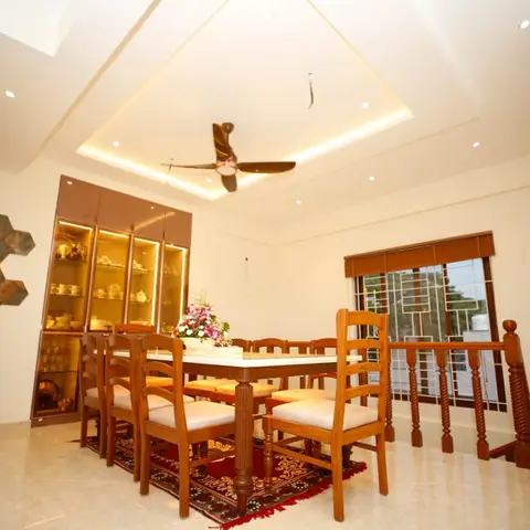 A dining room with an 8-seater carved wood table and chairs on a patterned red rug, a lit glass-front crockery cabinet, a hexagonal-tile wash-basin nook