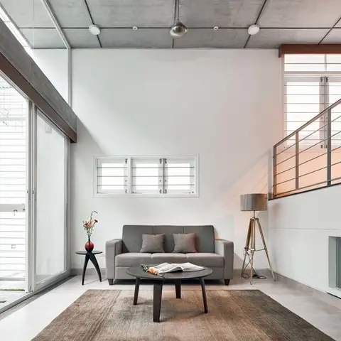 A double-height industrial-style living room with an exposed concrete beam ceiling, a grey sofa, a round black coffee table