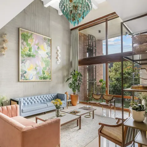 A double-height living room where a powder-blue buttoned leather sofa and a blush velvet channel-back sofa sit on a cream rug