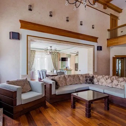 A double-height living room with a dark-wood-framed sectional sofa and glass-top coffee table in front of a stone fireplace mantel