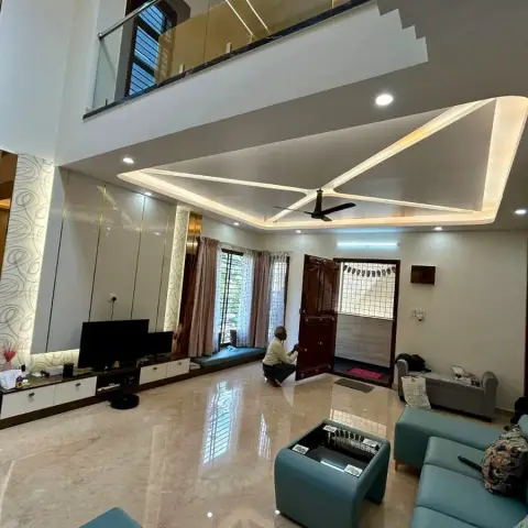 A double-height living room with a folded triangular POP ceiling raft lit along its edges, a TV wall of printed glass and mirror panels split by brass reveals