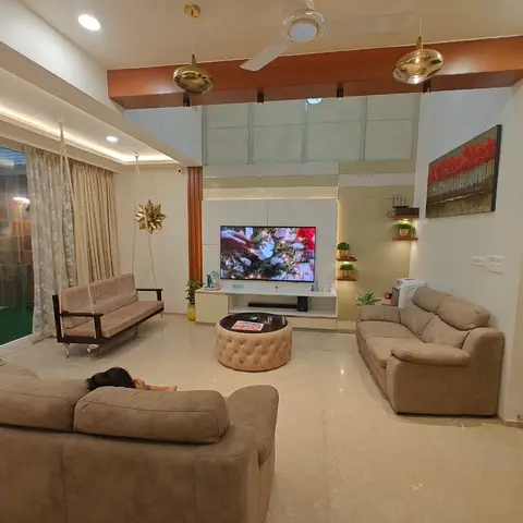 A double-height living room with a wood-framed TV wall, gold globe pendant lights, an indoor swing seat, and sliding doors opening to a private garden.