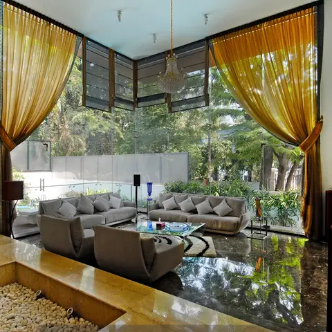 A double-height villa living room with floor-to-ceiling glazing onto a private garden and pool, gold silk drapery, a crystal chandelier