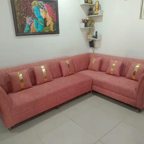 A dusty-rose channel-tufted L-shaped sofa with gold-striped cushions beneath a Radha-Krishna painting