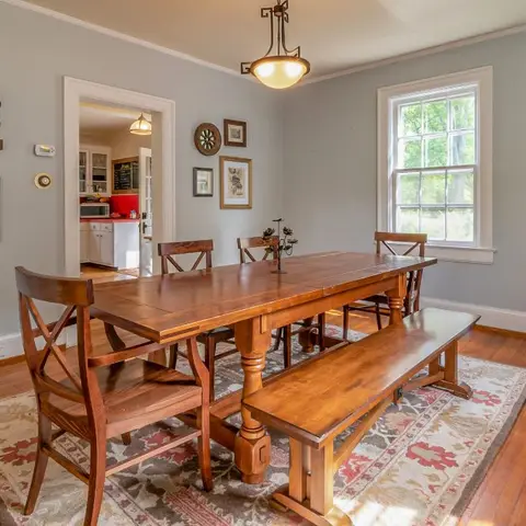 A farmhouse-style dining room with a long wood trestle table and bench seating on a floral rug, a gallery wall of framed art