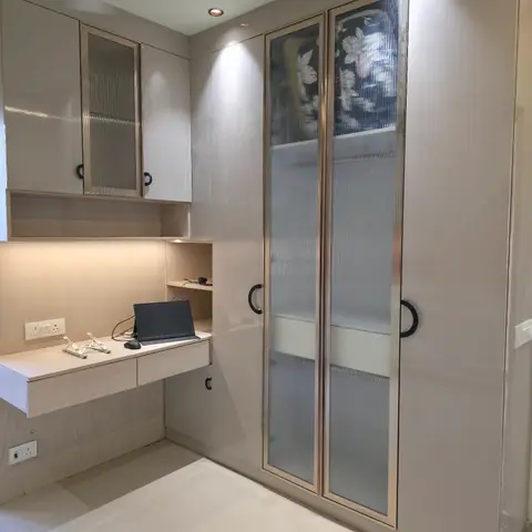 A floating study desk with a laptop stand built into a wood-veneer nook beside a floor-to-ceiling wardrobe with fluted glass and floral-print glass shutters.