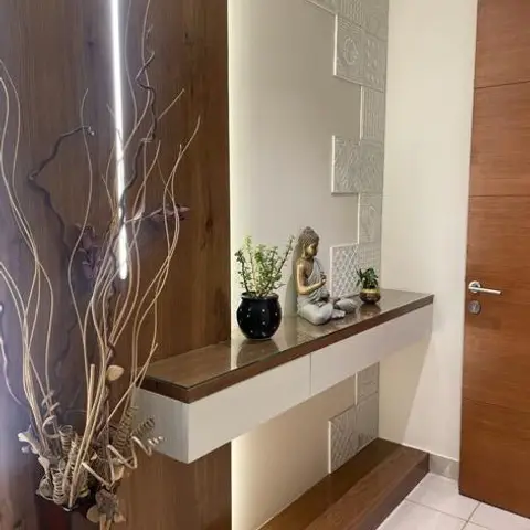 A floating wood-and-white console styled with a Buddha statue and dried botanicals against a backlit walnut panel and textured white relief tile.