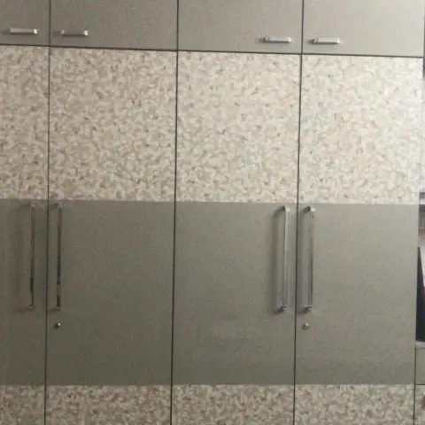 A floor-to-ceiling two-tone wardrobe wall in grey and granite-effect laminate with chrome bar handles, glimpsed beside a floral-sheeted bed.