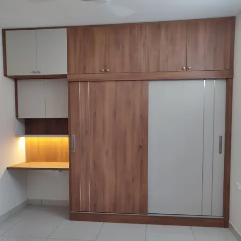 A floor-to-ceiling wood-and-white wardrobe with sliding doors sits beside a small built-in study desk with under-shelf task lighting