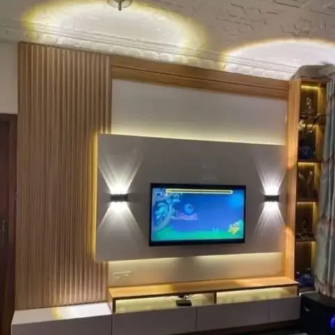 A fluted-wood TV feature wall with backlit wall sconces flanking the screen, beneath an arched carved cove ceiling, beside a lit glass crockery display.