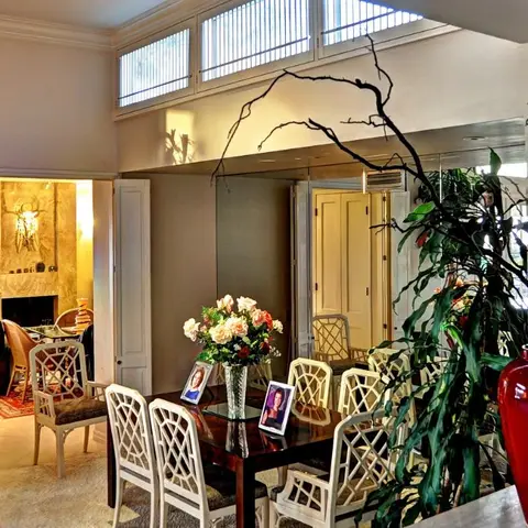A formal dining room with fretwork-back white chairs around a dark wood table, a tall red ceramic floor vase