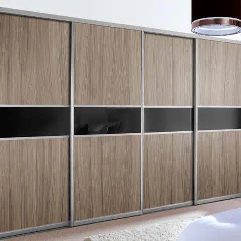 A four-panel wood-veneer sliding wardrobe with a black glass accent band and aluminium frame, beside a bed corner and a round pendant light.