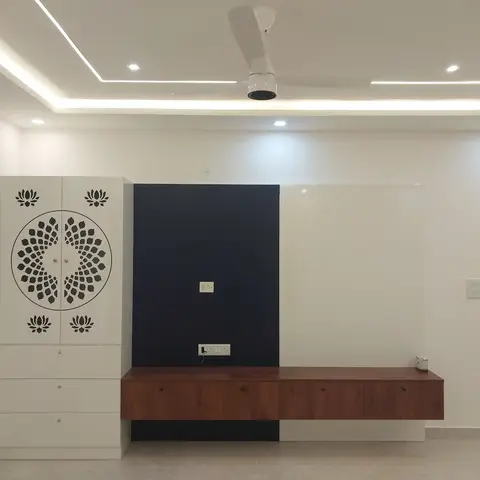 A freshly finished, unfurnished room with a lotus-motif carved wardrobe beside a navy-and-white two-tone TV feature wall and a floating wood console.