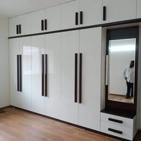 A full-height glossy white wardrobe wall with dark vertical pull handles and an integrated dresser mirror unit with drawers