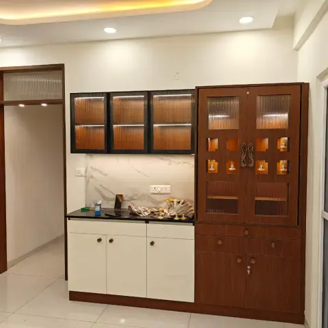 A full-height walnut pooja cabinet with reeded-glass shutters and a row of backlit brass diya inlays