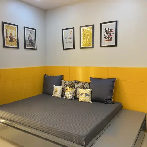 A girl's bedroom corner with a mustard-yellow upholstered wainscot wall behind a low platform bed, and a gallery wall of family photos and motivational prints
