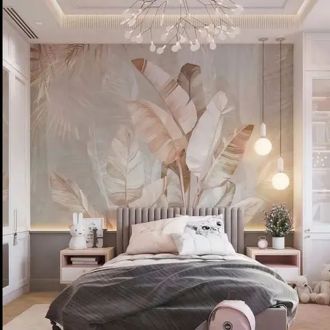 A girl's bedroom with a blush-toned tropical leaf mural wallpaper behind a channel-tufted grey headboard, twin globe pendant lights