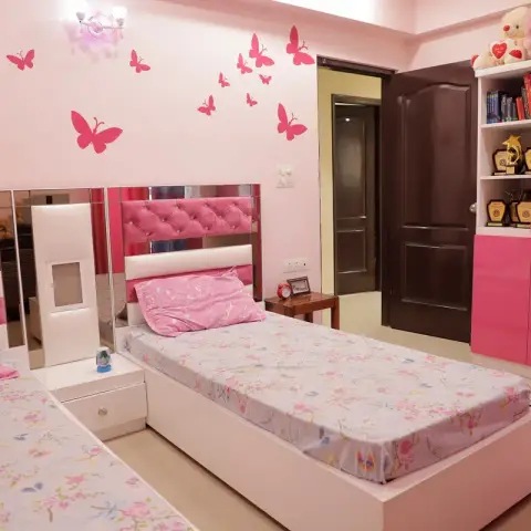 A girls' bedroom with twin beds against a mirrored, pink tufted headboard wall, pink butterfly wall decals