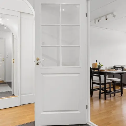 A glass-paned white door opens from a hallway into a combined dining and living area with a dark wood table and a light grey sofa